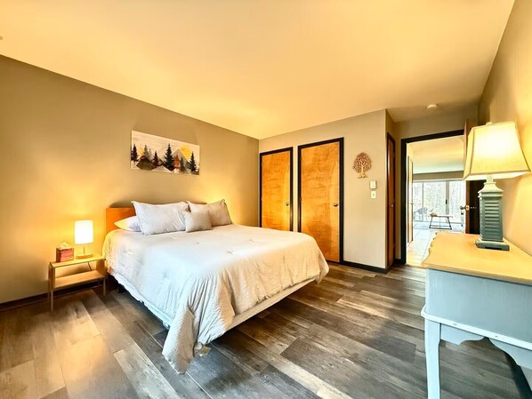 A bedroom with a bed, nightstands, a desk, and a door leading to a balcony. - Powder Days Retreat, Fireplace & Sugarbush Base (Warren)