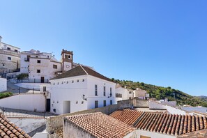 A white building with a clock tower, terracotta roof tiles, and a hillside in the background.