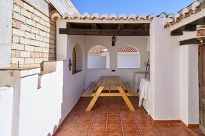 A narrow courtyard with a wooden table, white walls, tiled floor, and a tiled roof.
