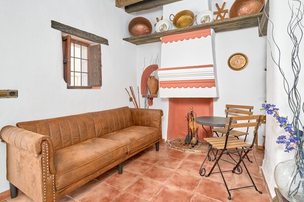 A room with a brown sofa, a dining table with chairs, a small window, and a decorative wall shelf.