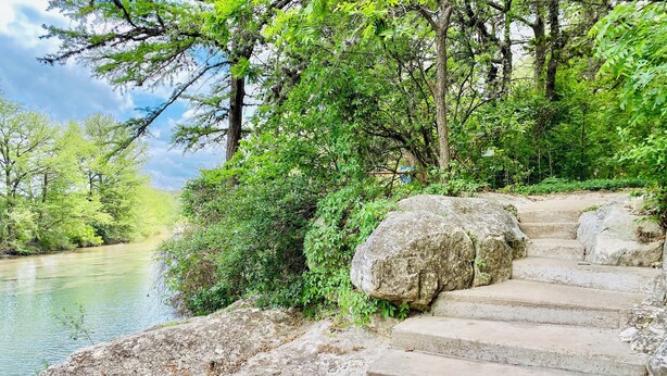 Un escalier en pierre menant à une rivière, entouré d’une végétation luxuriante et d’arbres.