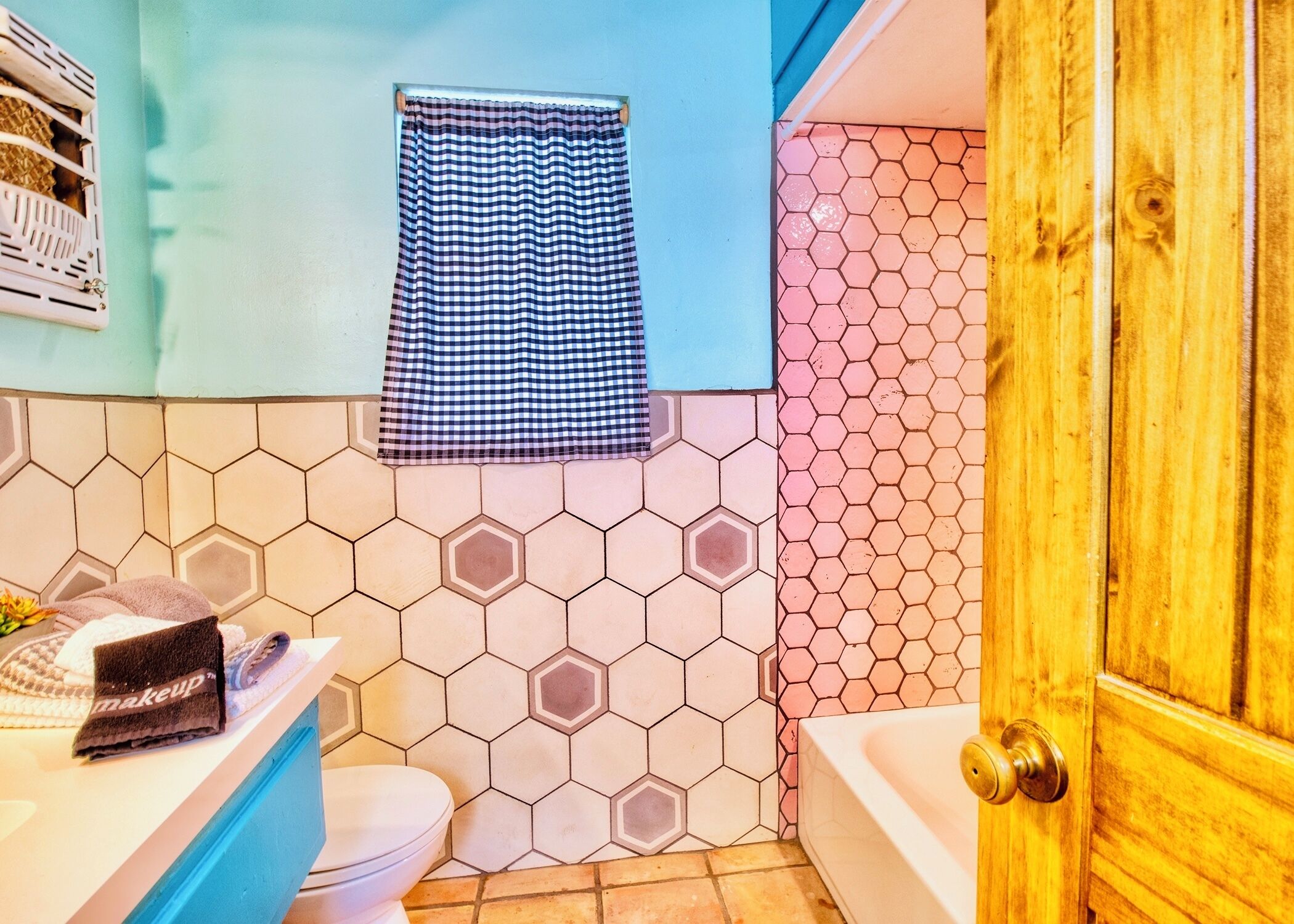 Un baño con un patrón de azulejos hexagonales, una toalla blanca y azul a cuadros, un inodoro blanco y una puerta de madera.