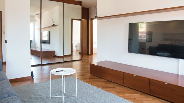 Una sala de estar moderna con un televisor de pantalla plana grande, piso de madera y una alfombra gris.