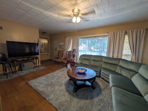 A living room with a television, sofa, armchair, and a dining table with a bowl.