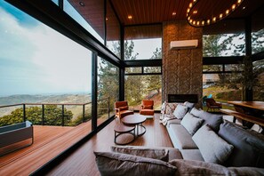 Un intérieur moderne avec une grande fenêtre, un plancher en bois, un mur d’accent en pierre et un coin salon avec un canapé et des fauteuils.