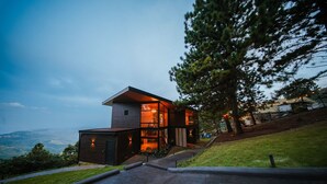 Una casa moderna de dos pisos con un balcón visible y un amplio ventanal con vistas a un paisaje pintoresco.