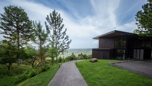 Una casa moderna con un camino de hormigón que lleva a un amplio ventanal con vistas a un paisaje pintoresco.