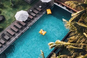 A pool with lounge chairs and umbrellas, surrounded by palm trees.