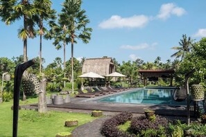 A pool area with lounge chairs, umbrellas, and a thatched-roof building.