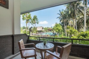 A balcony with a wooden table and chairs, overlooking a pool and lush greenery. - The Artini Dijiwa Ubud (Bali)