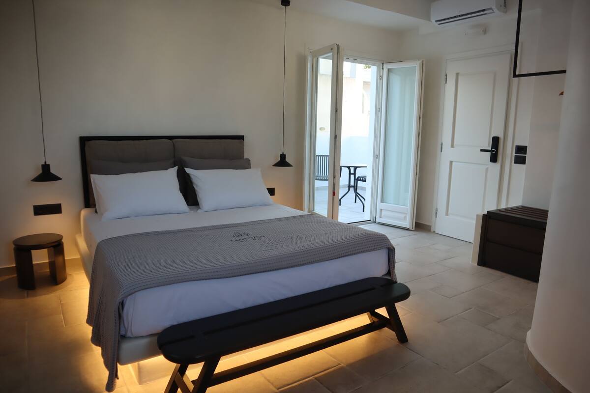 A neatly arranged bedroom with a large bed, bedside tables, a bench, and a view of the outside balcony.