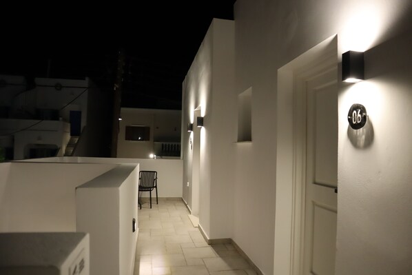 A narrow corridor with a bench, a door with a number plaque, and a wall-mounted light fixture. - Santozen Suites (Santorini)