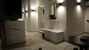 A modern bathroom with a white sink, a mirror, and wall-mounted lights. - Santozen Suites (Santorini)
