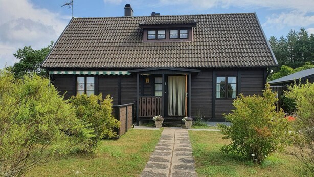 Une maison à deux étages, avec un toit recouvert de tuiles, un porche à l’avant et un chemin de pierre menant à l’entrée.