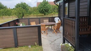 Une terrasse extérieure avec une table et des chaises en bois, entourée d’une clôture en bois et d’un espace jardin.