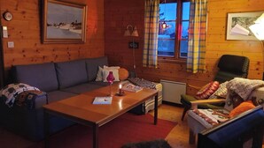 Une pièce confortable, aménagée comme un chalet, avec un intérieur en bois, un canapé, une table avec un livre, une chaise et une fenêtre avec des rideaux.
