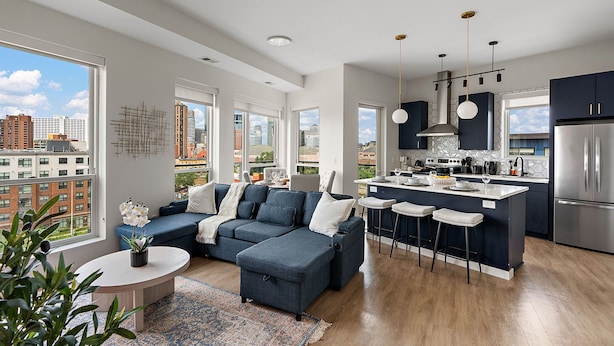 A modern apartment with a living area, kitchen, and dining space. It features large windows, a blue sofa, and a kitchen island with bar stools. - Luxury 2Bd Condo DT Minneapolis, Minutes From Convention Center & US Bank Arena (Minneapolis)