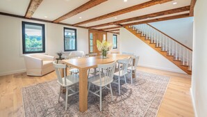 A spacious dining area with a wooden table and chairs, a large rug, and a staircase leading to an upper level.