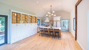 A spacious kitchen with white cabinetry, a central island with bar stools, and a modern chandelier.