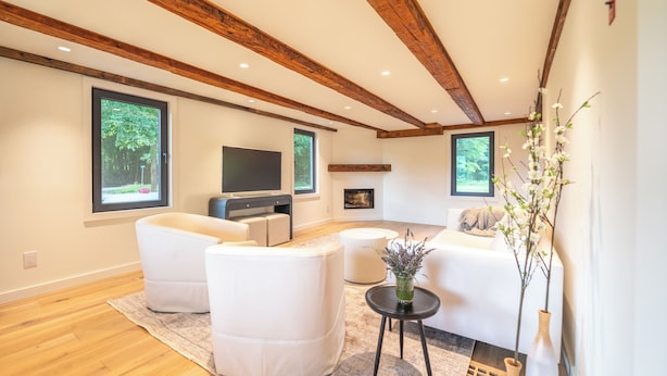 A modern living room with wooden beams, a flat-screen TV, white sofas, and a fireplace.