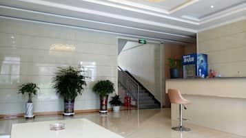 Um hall moderno com balcão de recepção, plantas em vasos, escada e piso limpo e lustroso.