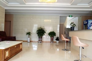 Un hall de hotel con mostrador de recepción, zona de estar y plantas en macetas.