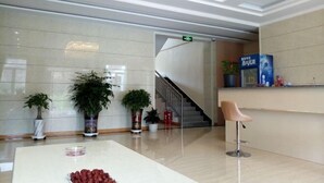Un vestíbulo con mostrador de recepción, plantas en macetas, una escalera y una gran mesa blanca.