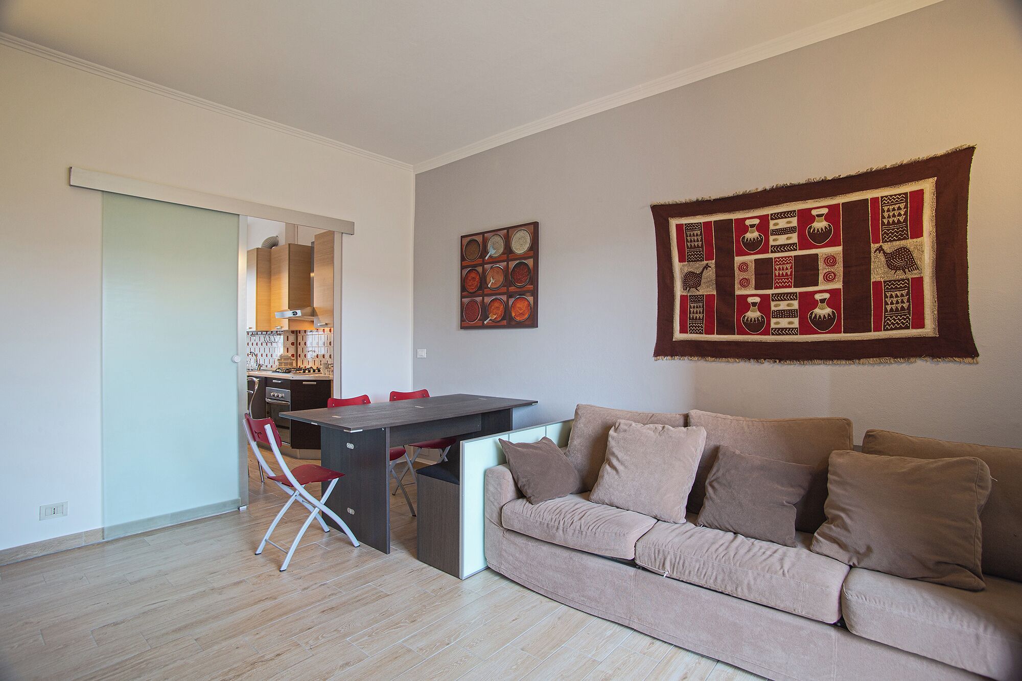 Una sala de estar moderna con un sofá, una mesa de comedor y sillas. Se ve una cocina a través de una puerta abierta.