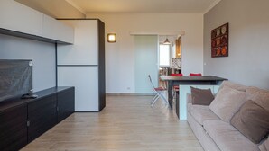 A modern living room with a sofa, a TV, and a kitchen in the background.