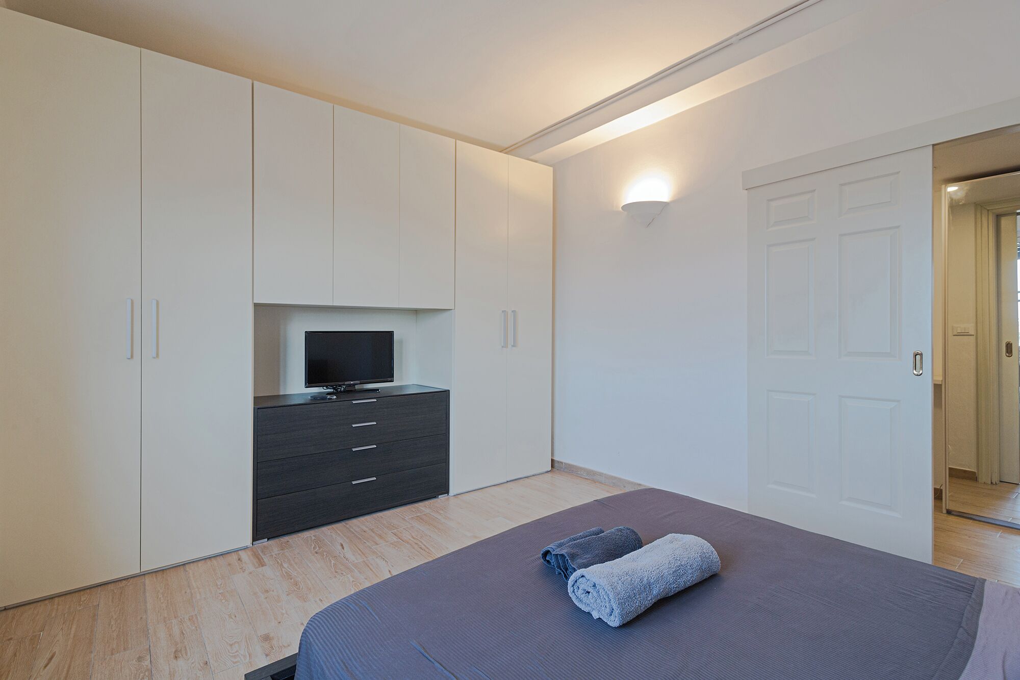 Una camera da letto con un letto, una televisione su un comò e una porta.