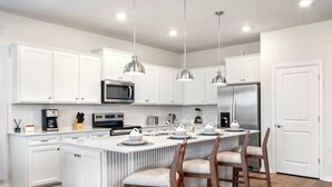 A modern kitchen with white cabinetry, stainless steel appliances, and a central island with bar stools.