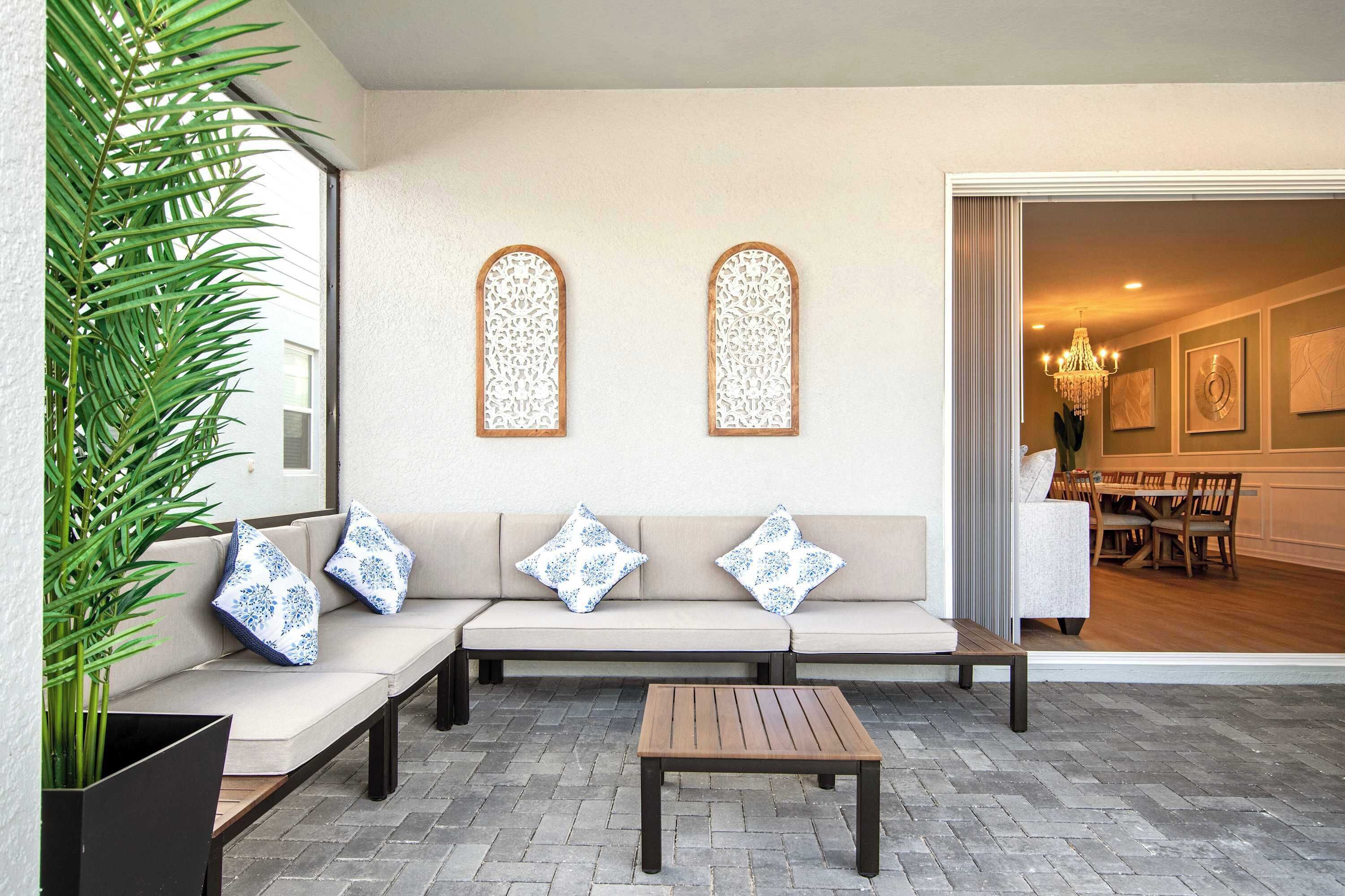 Un espace extérieur moderne aménagé avec un canapé, deux tables en bois et des panneaux muraux décoratifs.
