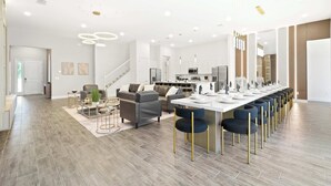 Un vaste espace de vie comprenant une longue table à manger, des meubles modernes et un escalier menant à un niveau supérieur.