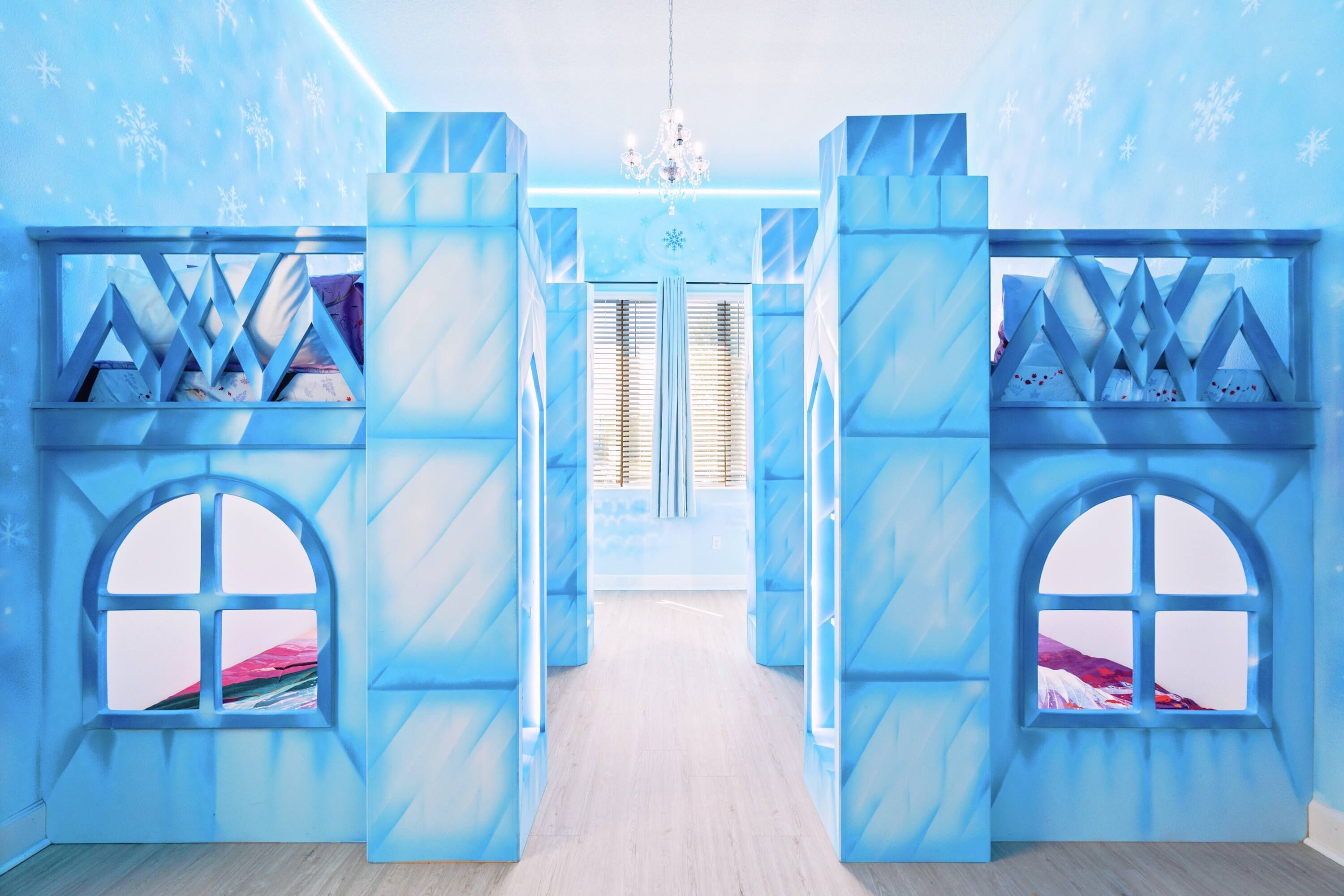 Una habitación con decoración azul, que incluye una cama con cabecera blanca, una ventana con vistas a un paisaje nevado y una araña.