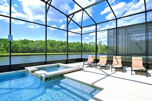 Una piscina con paredes de cristal, sillas de descanso y vistas a un lago y un bosque.