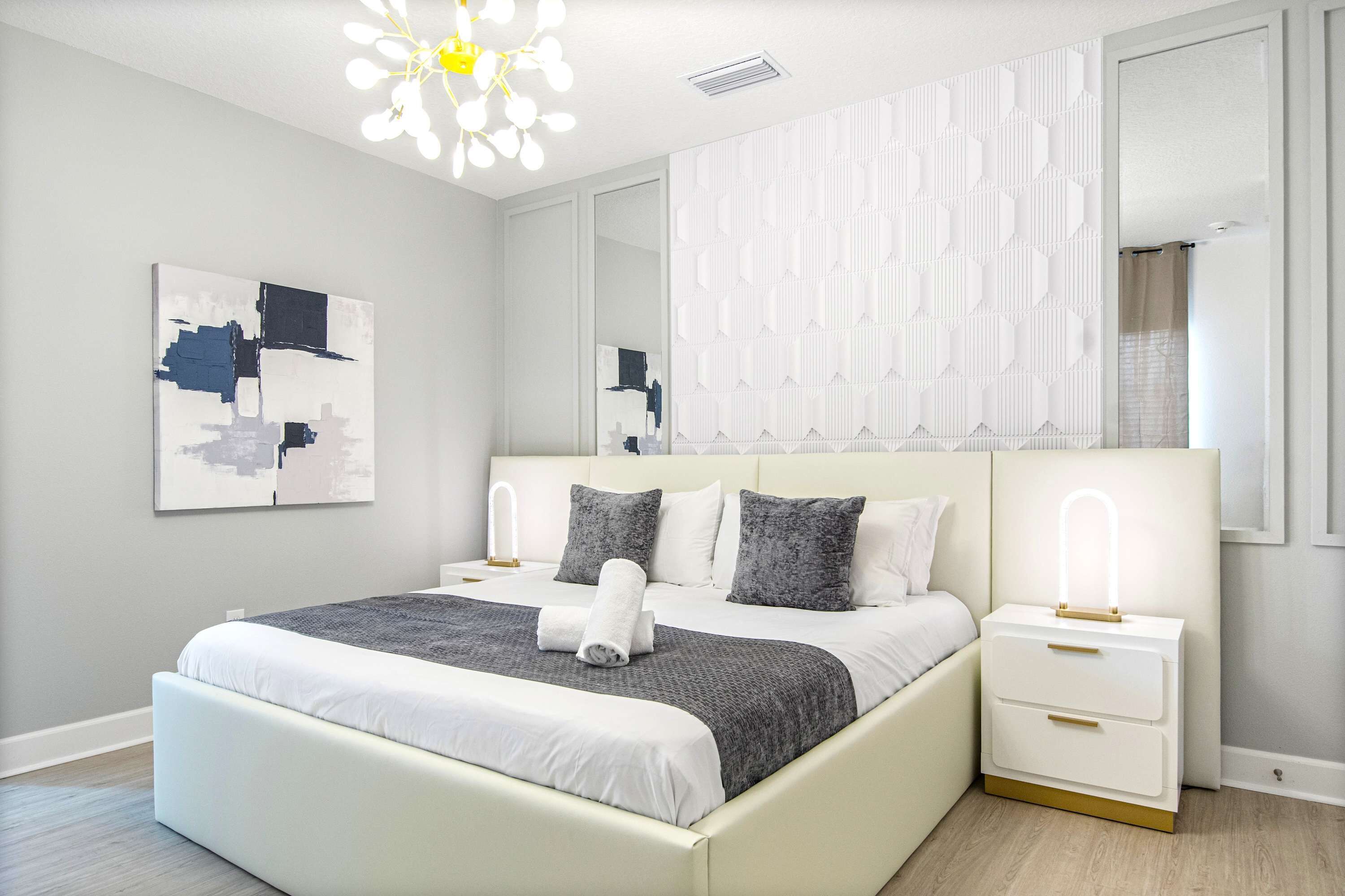 A modern bedroom with a large bed, bedside tables, a mirror, and a ceiling light fixture.
