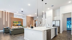 A modern kitchen with a central island, white cabinetry, and stainless steel appliances. - Themed Kids' Rooms, Pool & Game Loft Near Disney (Kissimmee)