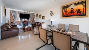 A modern living room with a brown leather sofa, a dining table with chairs, a flat-screen TV, and a painting of a sunset scene. - Casa Maru (Tequisquiapan)
