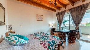 A bedroom with a bed, a small table, two chairs, a chandelier, and a view of the outside. - Casa Maru (Tequisquiapan)