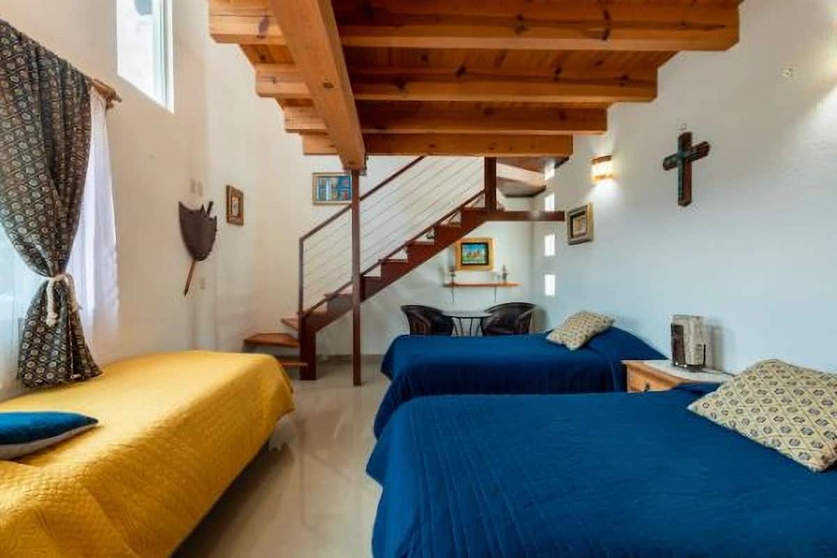Ein Zimmer mit zwei Betten, Holzbalken, einer Treppe und einem Kreuz an der Wand.
