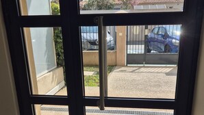 On aperçoit, à travers une porte vitrée, un parking où une voiture bleue est garée au fond.