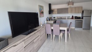 Une cuisine moderne dotée d’un grand téléviseur à écran plat, de meubles en bois et d’un coin repas avec une table et des chaises.