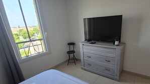 Une chambre à coucher comprenant un lit, une commode, un téléviseur et une fenêtre donnant sur un paysage verdoyant.