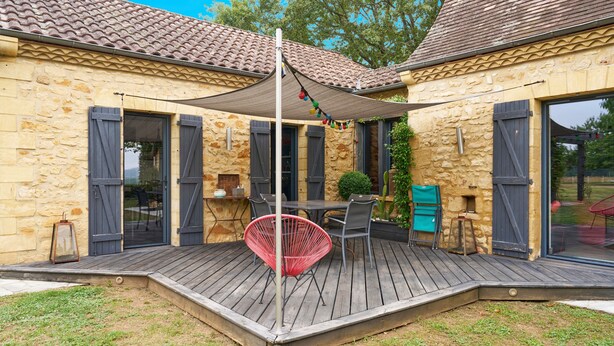 Un edificio de piedra con terraza de madera, mobiliario exterior y una pérgola.