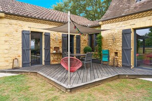 A stone building with a wooden deck, outdoor furniture, and a pergola.