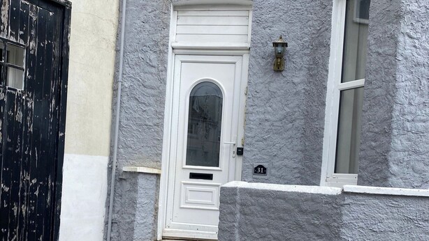 A white door with a small window above it, a black gate to the left, and a house number '31' on the wall.