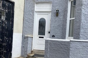 Une porte blanche avec une petite fenêtre au-dessus, un portail noir sur la gauche et le numéro de la maison, « 31 », peint sur le mur.