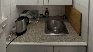 A compact kitchen with white cabinets, a stainless steel sink, a kettle, a toaster, and a dish rack.