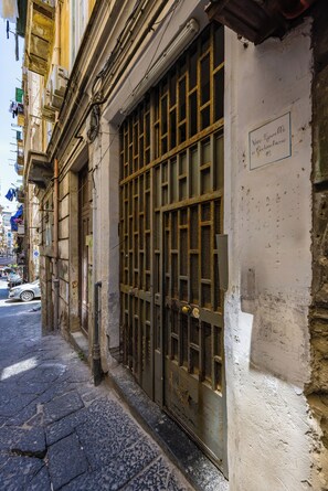 A narrow street with a building featuring a metal gate and a sign indicating a historical site.