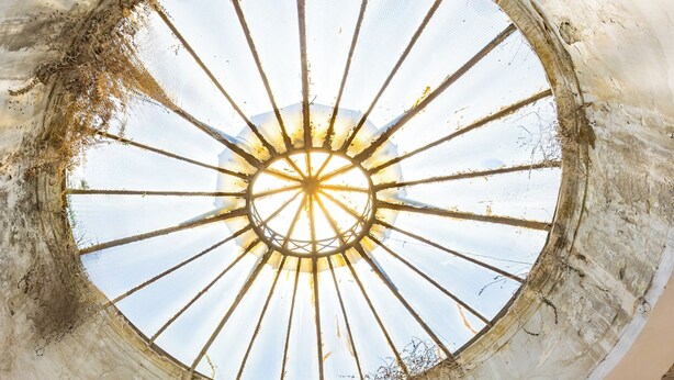 Une lucarne circulaire ornée d’un motif central en forme de rayons de soleil, une porte rouge et un mur à texture.
